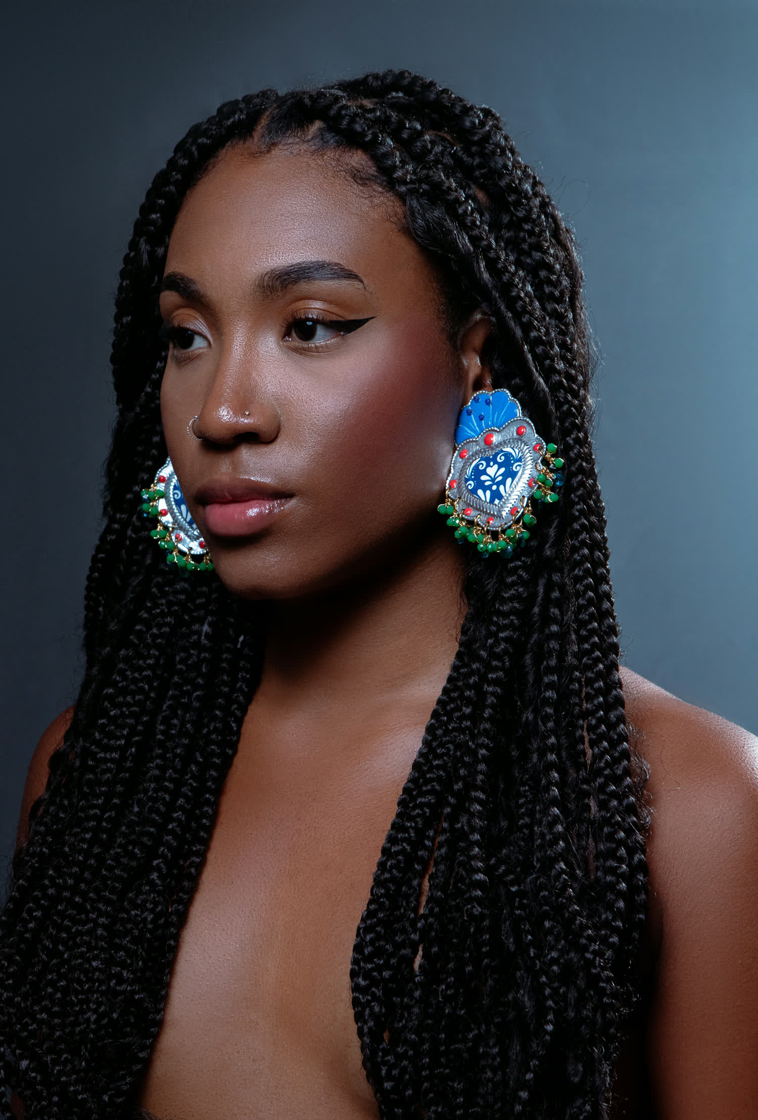 Modelo de perfil con aretes de gran formato pintados en azul y rojo con remate de cuentas verdes