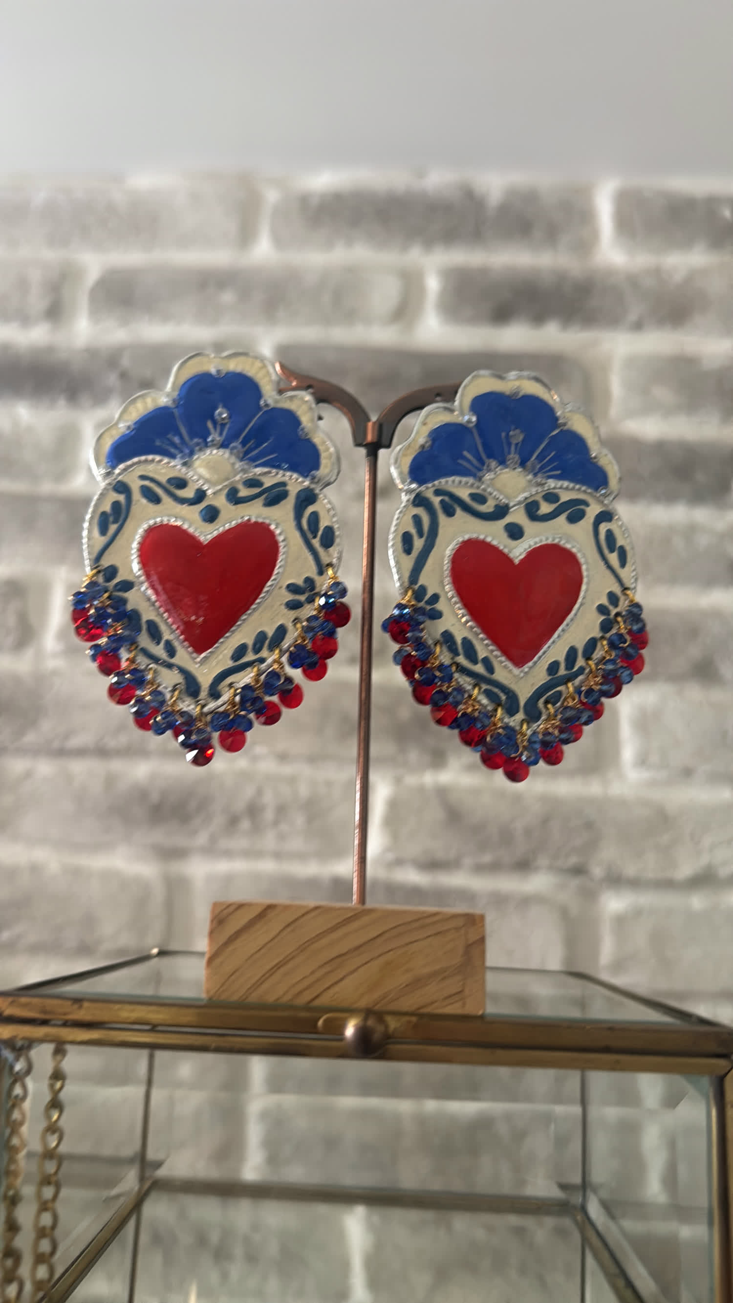 Aretes pintados a mano con un corazón rojo y flores azules sobre fondo crema