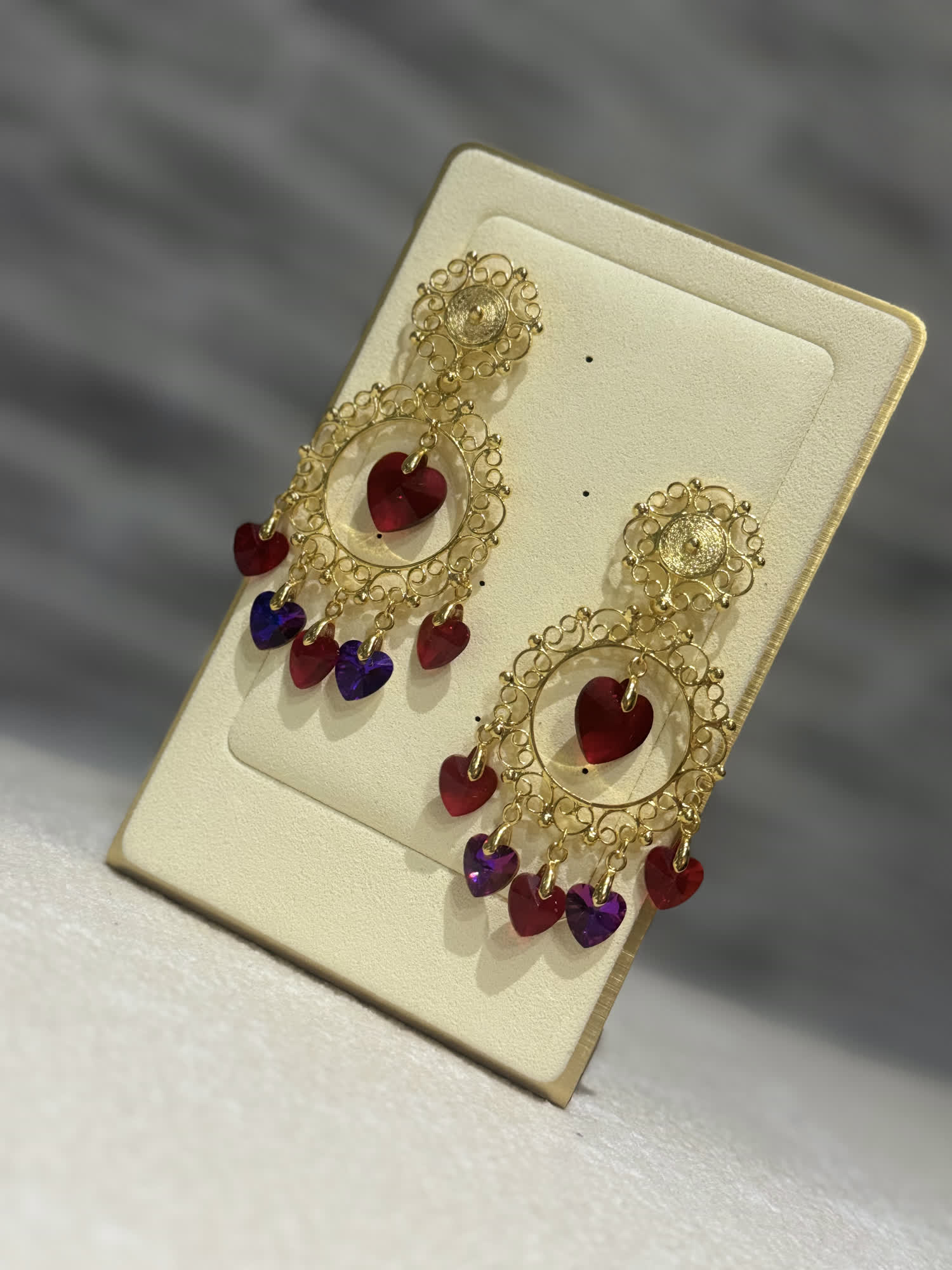 Aretes de filigrana dorada con corazones de cristal rojo y violeta colgando